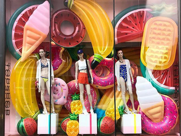 A store window display with oversized inflatable elements to create a summery theme