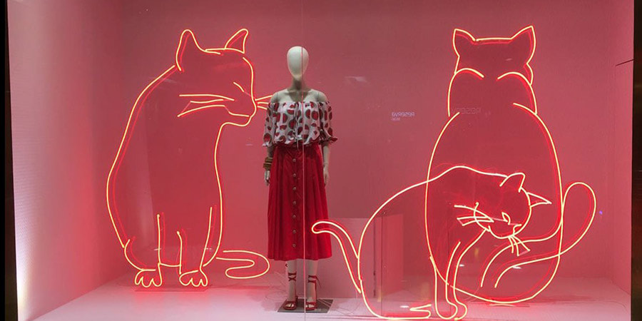 A shop window display using LED neon signs shaped as three cats.
