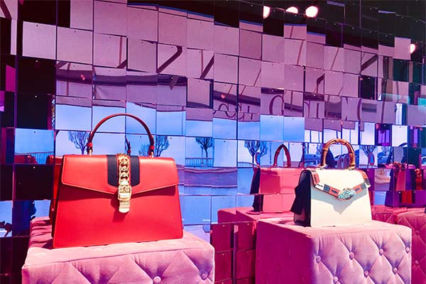 A photograph of two fashion brand bags with shimmerwall visual merchandising background.