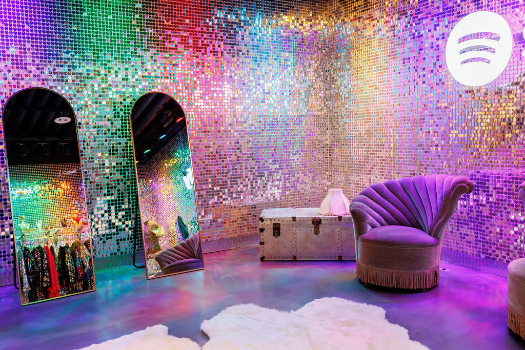 A silver sequin backdrop, lit up in multiple colours to create a rainbow effect.